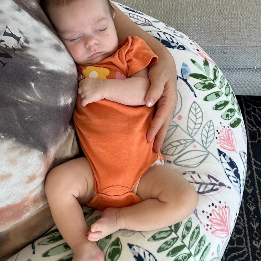 Baby in an orange onesie sleeping on a floral-patterned cushion