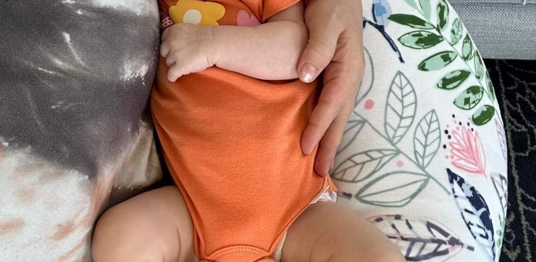 Baby being supported by Luna Lullaby nursing pillow in mom's lap.