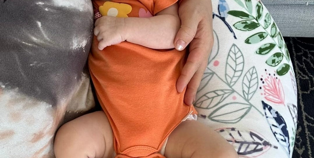 Baby in an orange onesie sleeping on a floral-patterned cushion