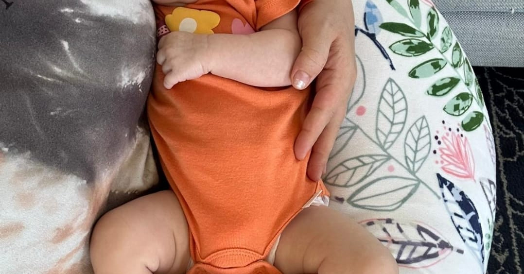 Baby in an orange onesie sleeping on a floral-patterned cushion