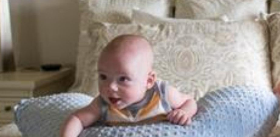 Baby sitting on a textured pillow in a bedroom setting