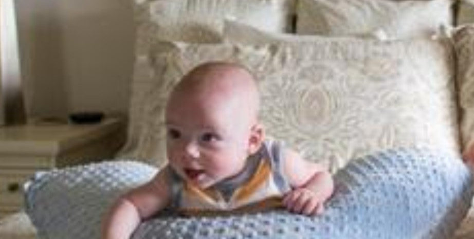 Baby sitting on a textured pillow in a bedroom setting
