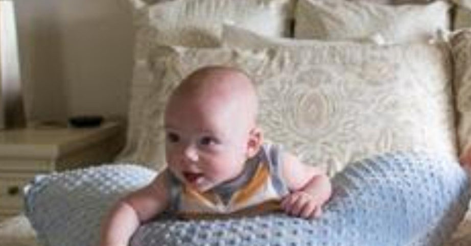Baby sitting on a textured pillow in a bedroom setting