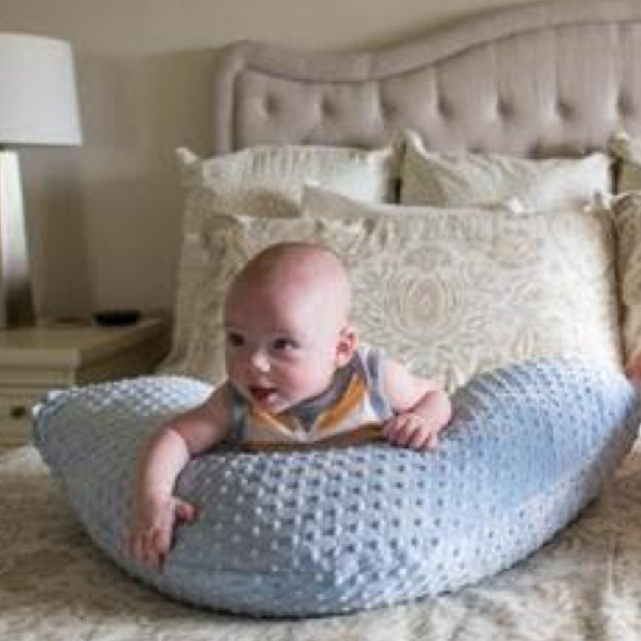 Baby sitting on a textured pillow in a bedroom setting