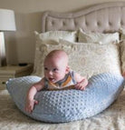 Baby sitting on a textured pillow in a bedroom setting