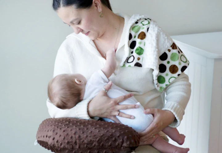 Woman breastfeeding a baby with a brown pillow on a light background
