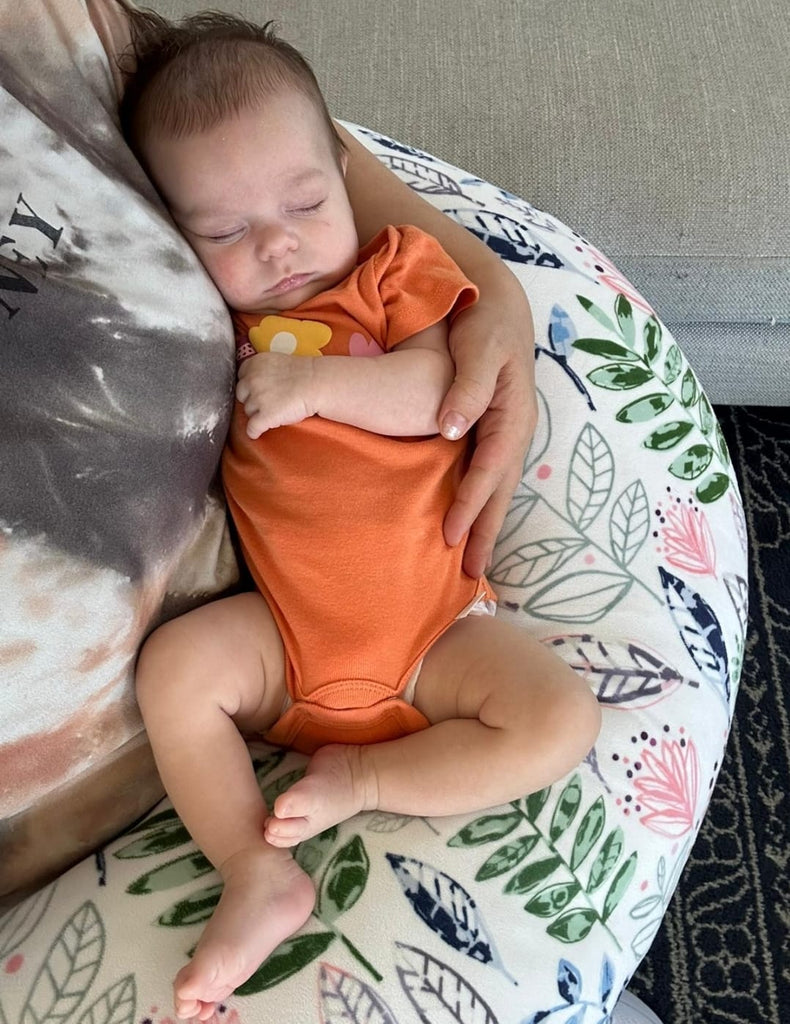 Baby in an orange onesie sleeping on a floral-patterned cushion